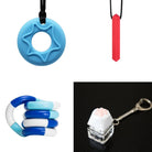 A collage of the "2 Chew Necklaces + 2 Fidget Toys Bundle" featuring: Top left is a blue star-shaped chew necklace, top right is a red stick-shaped chewable pendant, bottom left is a wavy blue and white twistable fidget toy, and bottom right is a paw keyboard fidget keychain with a soft paw-like button.